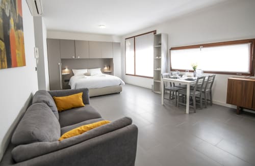Moderno monolocale a Ferrara con divano grigio, letto bianco, zona pranzo e vista sulla città
