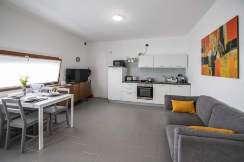 Moderno monolocale a Ferrara con cucina a vista, tavolo da pranzo, divano grigio e opere d'arte arancioni