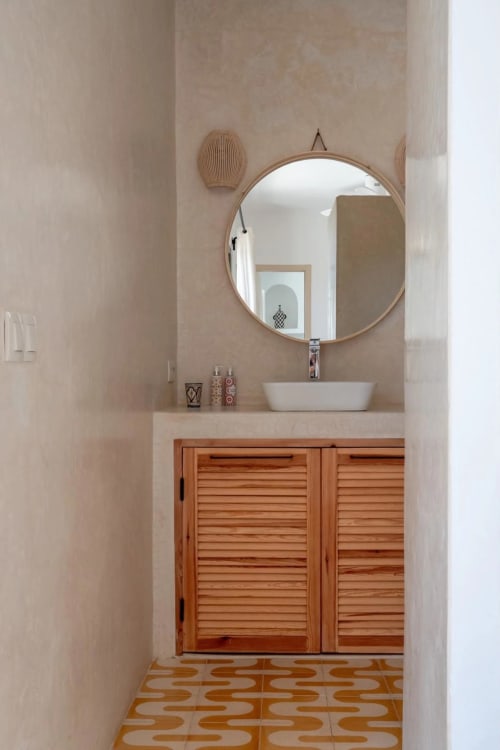 Salle de bains épurée au Domaine Belhazar à Essaouira : miroir rond, lavabo blanc, meuble en bois et carrelage géométrique