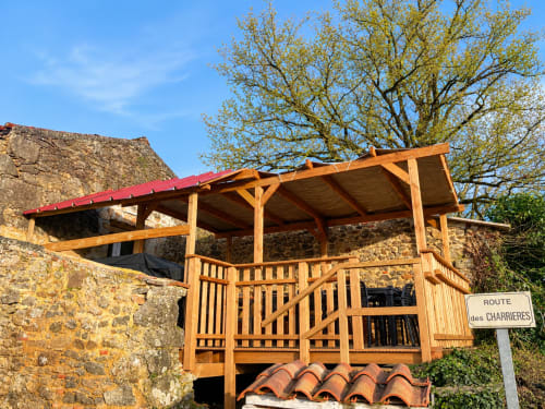 Tonnelle en bois à toit rouge du gîte Le Petit Moulin à Pouzauges, bâtiment en pierre en arrière-plan
