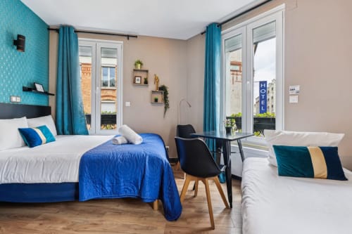 Chambre moderne à la Résidence Aurmat avec deux lits, touches turquoise et vue sur balcon parisien
