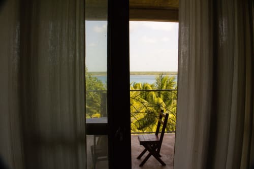 Vista de la terraza del hostal Cayuco Maya en Bacalar con palmeras, laguna y silla de descanso con vista al lago