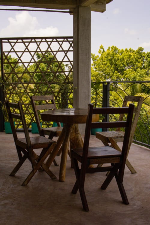 Sillas de madera y mesa redonda en terraza con vista a exuberante vegetación en el hostel Cayuco Maya, Bacalar México