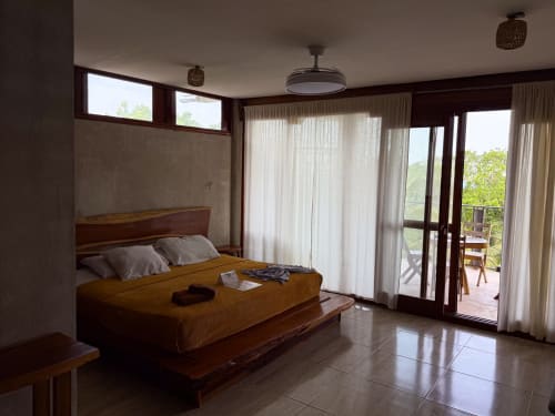 Amplia habitación con vistas al lago en el hostel Cayuco Maya de Bacalar con cama de madera, acceso a terraza y comodidades modernas