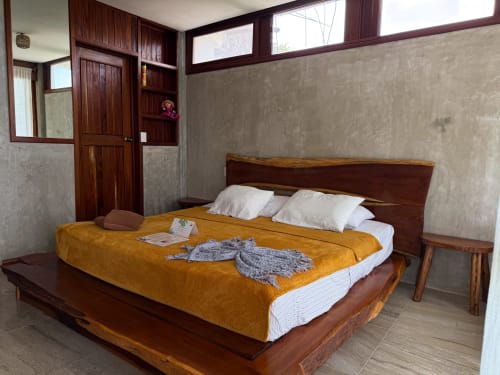 Cama de madera con ropa de cama amarilla y almohadas blancas en habitación del hostal Cayuco Maya, Bacalar México