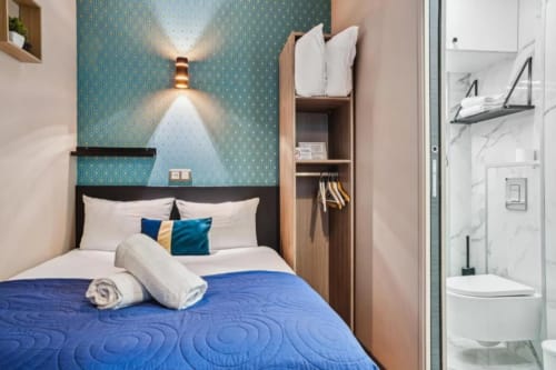 Modern hotel bedroom at Résidence Aurmat Paris with blue accent wall, white bedding, and integrated bathroom in