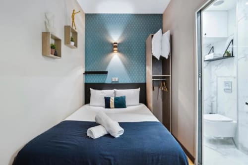 Compact bedroom at Résidence Aurmat boutique hotel Paris with blue accent wall, white bedding, and ensuite bathroom