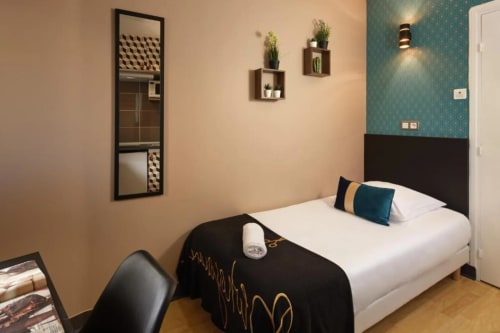 Modern hotel bedroom at Résidence Aurmat Paris Boulogne with teal accent wall, potted plants, and black bed frame