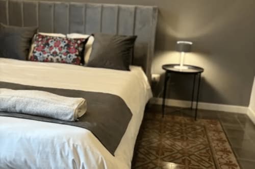 Modern bedroom at Moon Rooms By Celeste in Catania with gray headboard, floral pillow, and bedside table lamp