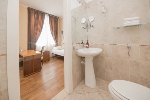 Bagno moderno con lavabo su colonna e wc al Green Hotel Poggio Regillo di Frascati, con camera da letto e scrivania visibili sullo sfondo