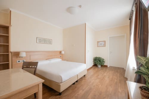 Spaziosa camera d'hotel al Green Hotel Poggio Regillo con letto matrimoniale, arredi in legno e vista sul giardino a Frascati