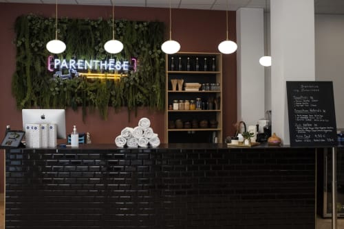 Parenthèse spa reception desk with neon sign, green plant wall, pendant lights, and black brick counter at Résidence Aurmat