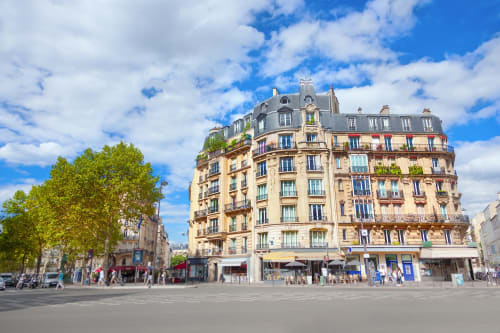 Immeuble haussmannien classique à Boulogne-Billancourt avec façade en pierre blonde, toit mansardé et café au rez-de-chaussée par beau temps