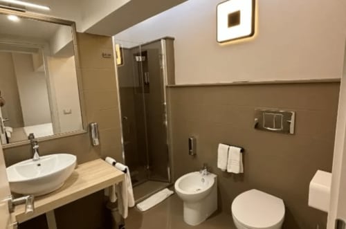 Modern bathroom at Moon Rooms By Celeste in Catania with curved sink, toilet, bidet, and dark tiled walls