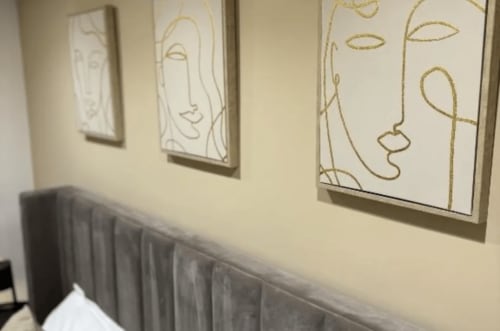 Modern line art portraits in gold on cream wall above gray headboard at Moon Rooms hotel, Catania