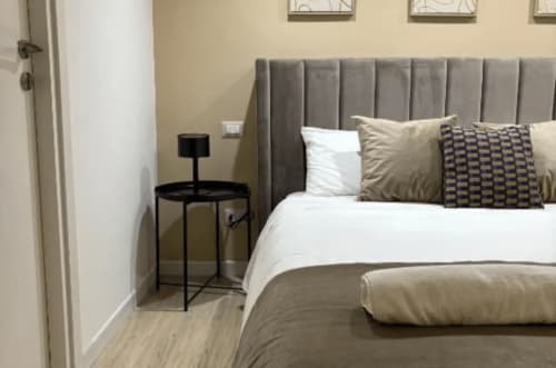 Modern bedroom at Moon Rooms By Celeste in Catania with gray upholstered bed, white linens, and minimalist black nightstand