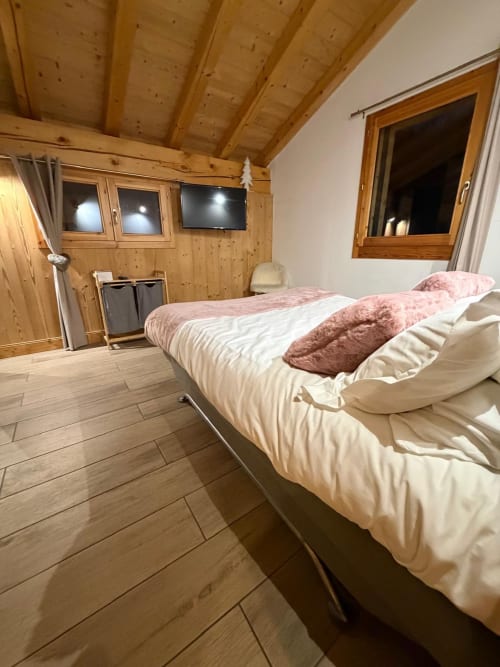 Chambre moderne aux Chalets d'Aline à La Plagne avec poutres apparentes, lit aux oreillers roses, téléviseur et parquet