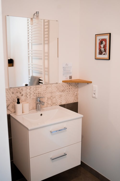 Modern bathroom vanity with patterned tile backsplash at Résidence des Sables, Mably apartment