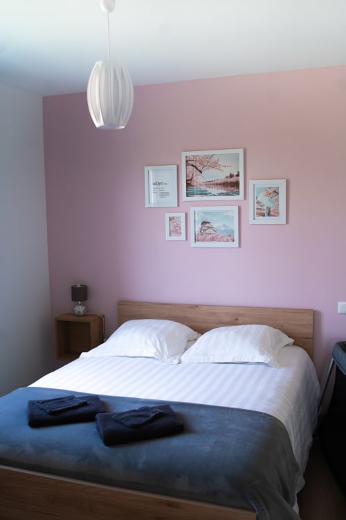 Modern bedroom at Résidence des Sables Tokyo apartment with pink walls, white pendant light, wood bed frame, and gallery wall