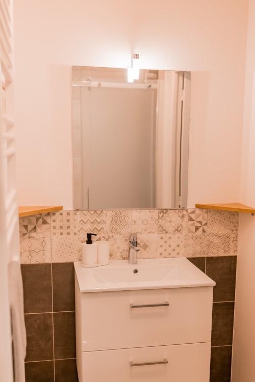 Modern bathroom vanity with decorative tile backsplash, white sink, and mirror at Résidence des Sables apartment