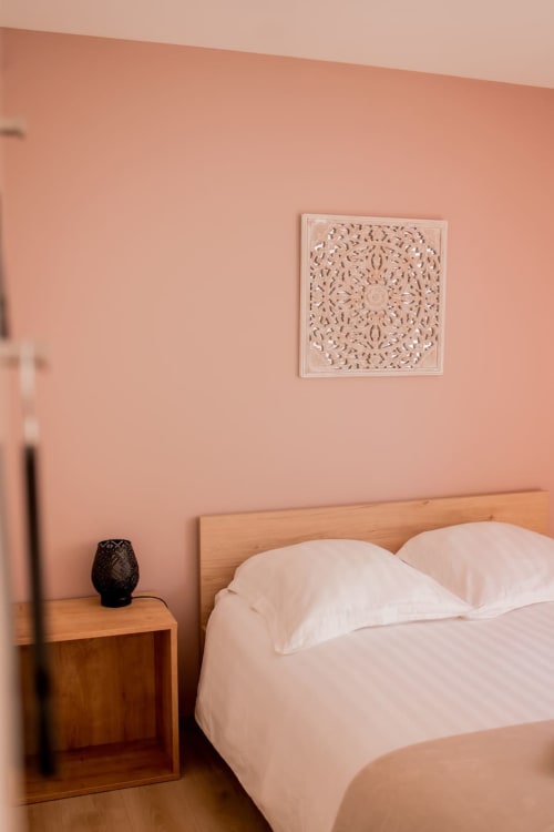 Bedroom in Résidence des Sables apartment with pink walls, wooden bed, white pillows, nightstand, and ornate wall art