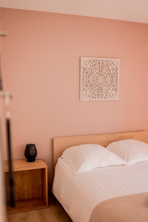 Bedroom at Résidence des Sables Mably with terracotta pink walls, wooden bed, white linens, and decorative carved panel