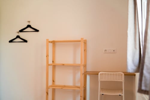 Minimalist apartment room at Résidence des Sables with wooden shelving, black hangers, white chair, and cream walls
