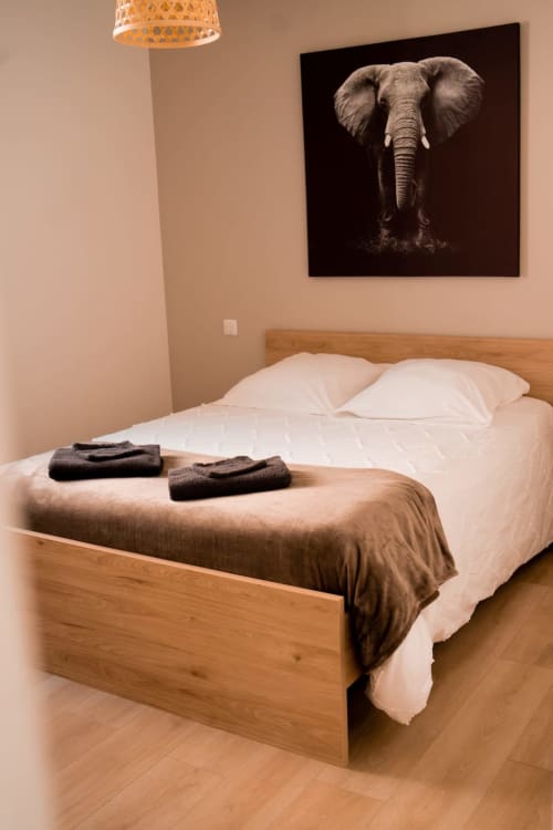 Bedroom with wooden bed, white pillows, brown throw blanket, woven pendant lamp, and elephant artwork at Résidence des Sables