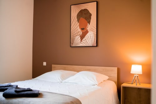 Modern bedroom at Résidence des Sables with wooden bed, white pillows, warm lighting, and contemporary portrait artwork on