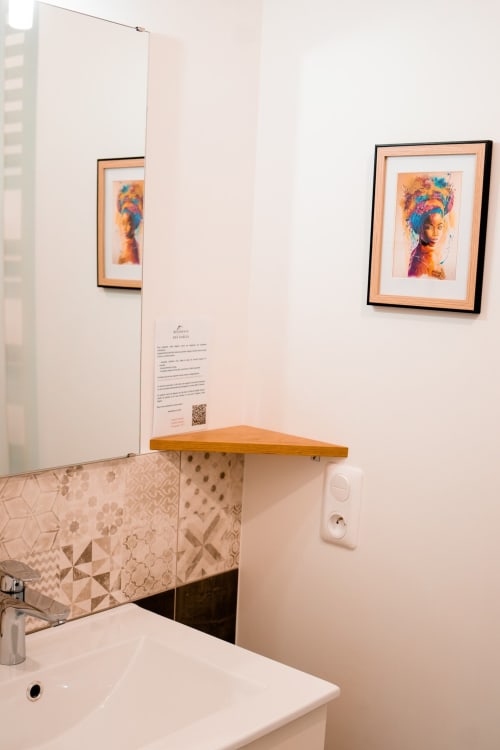 Modern bathroom with colorful portrait artwork, wooden shelf, patterned tile backsplash in Résidence des Sables apartment