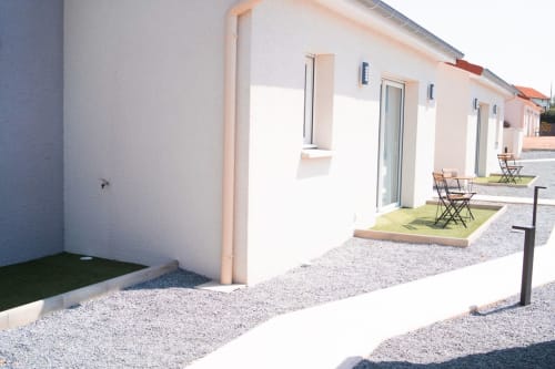 Row of modern apartment units at Résidence des Sables with terraces, gravel courtyard, and green outdoor seating areas in