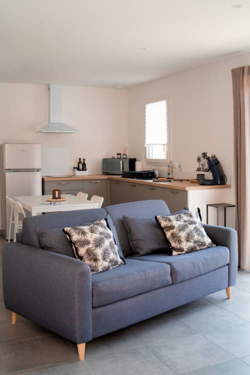 Modern open-plan studio apartment at Résidence des Sables with blue sofa, equipped kitchen, dining area and pool view window