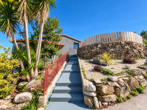 Casita El Román con vistas al mar en Baiona, camino de piedra y jardines exuberantes bajo cielo despejado