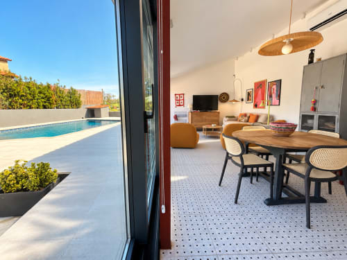 Interior moderno de cabaña con vistas al mar, mesa de comedor, asientos naranjas, lámpara colgante de madera y terraza con piscina en Holibai Baiona