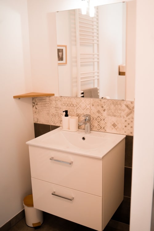 Modern bathroom vanity with white sink cabinet, patterned tile backsplash, and mirror at Résidence des Sables apartment in