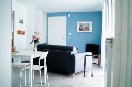 Modern apartment living area in Résidence des Sables, Mably with blue accent wall, black sofa, dining table and kitchenette