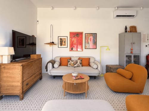 Sala de estar moderna en la casita El Román de Baiona con sofá beige, silla naranja, muebles de madera y vistas al mar
