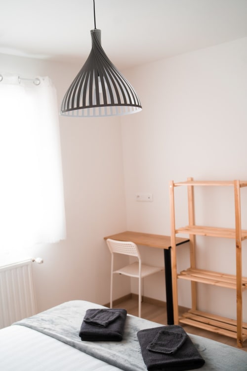 Modern bedroom at Résidence des Sables with pendant light, wooden shelving, and black towels on bed