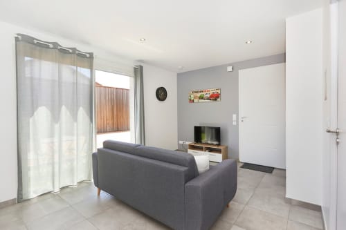 Modern living room in Appartement 4-Rome at Résidence des Sables, Mably, with gray sofa, TV, and access to inner courtyard