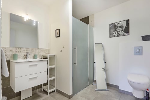 Modern bathroom in Résidence des Sables apartment with white vanity, mirror, shower, toilet, and contemporary decor