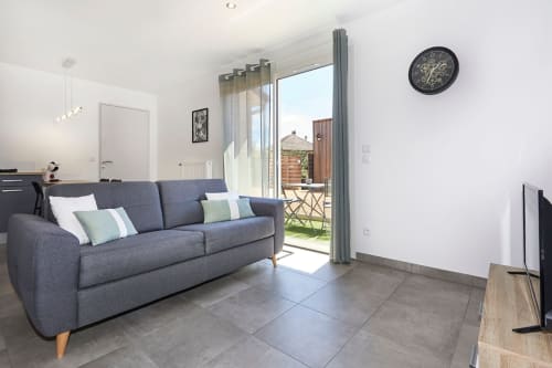 Modern living room with gray sofa, terrace doors, and inner courtyard view at Résidence des Sables, Mably apartment