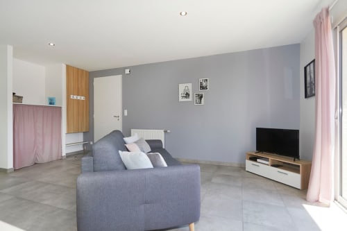 Modern apartment living room with gray sofa, TV, and kitchenette at Résidence des Sables in Mably