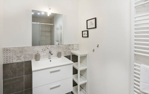 Modern bathroom in Résidence des Sables apartment with white vanity, patterned tile backsplash, and mirror with lighting