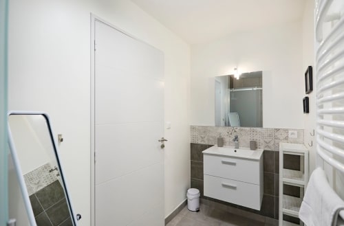 Modern bathroom at Résidence des Sables Mably with white vanity, tiled backsplash, mirror, and heated towel rack