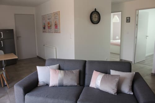 Modern living room in Appartement 3 at Résidence des Sables, Mably with gray sofa, decorative pillows, and clock on wall