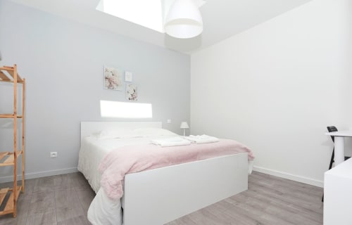 Bright modern bedroom at Résidence des Sables in Mably, France, featuring white bed with pink throw, minimalist décor, and
