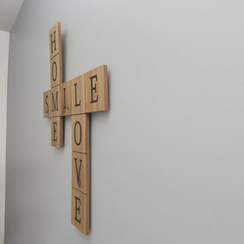 Wooden cross with 'SMILE LOVE' text on white wall at Résidence des Sables apartment in Mably