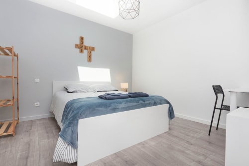 Modern bedroom at Résidence des Sables, Mably with white bed, blue bedding, wooden furniture, and geometric ceiling light
