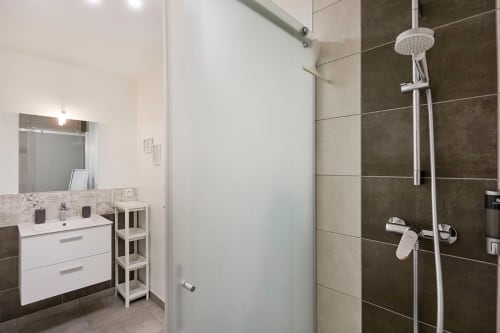 Modern bathroom with dark tile shower and white vanity at Résidence des Sables apartment in Mably