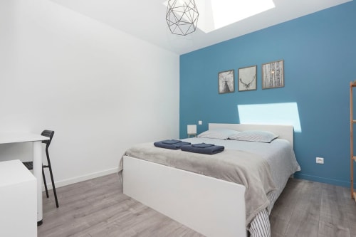 Modern bedroom at Résidence des Sables, Mably with blue accent wall, white bed, desk, and geometric ceiling light